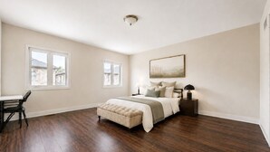 Un dormitorio con una cama grande, dos ventanas, un escritorio y una silla.