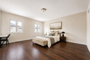 A bedroom with a large bed, two windows, a desk, and a chair.