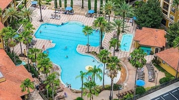 A large swimming pool surrounded by palm trees and lounge chairs, with a building in the background.