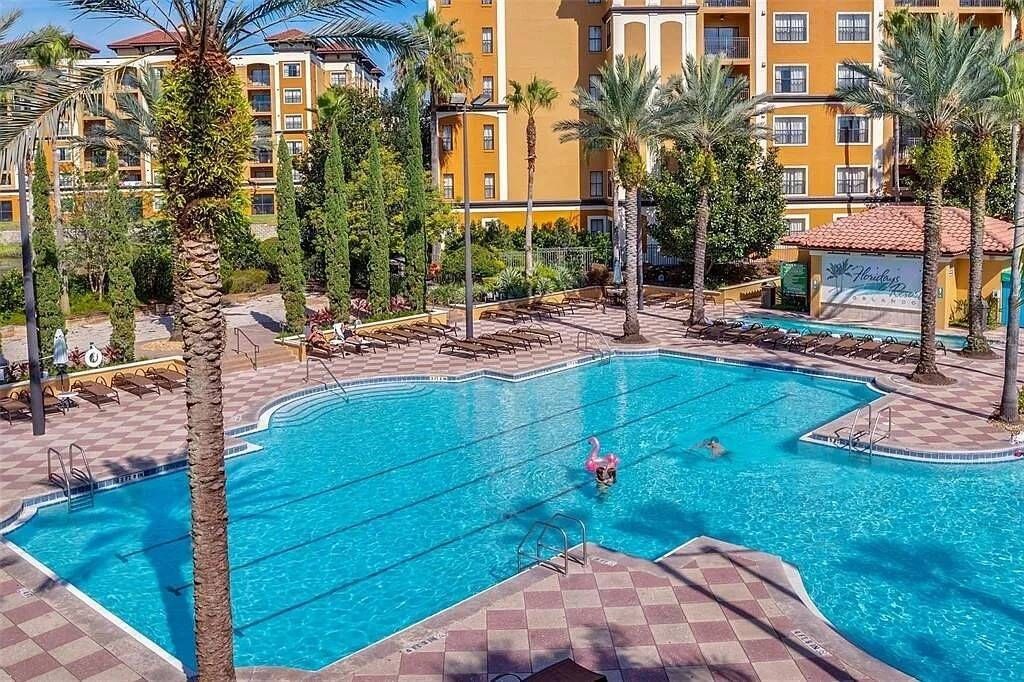Piscina con sillas de descanso y palmeras, rodeada por un edificio de hotel.