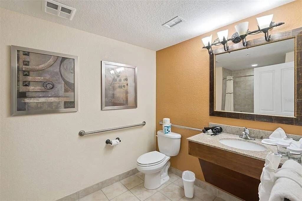 Un bagno con il water, un lavandino, uno specchio e due quadri appesi alla parete.
