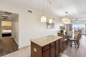 A modern kitchen with a central island, dining area with chairs, and a view of the outdoors. - 3BR Resort Suite on I-drive + Pools (Orlando)