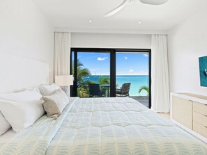 A bedroom with a bed, a nightstand, a lamp, and a view of the ocean through large glass doors. - Breathtaking Beachfront Suite in Simpson Bay (Simpson Bay)