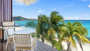 Ein Balkon mit Grill, weißen Korbstühlen und Blick auf Strand und Meer.