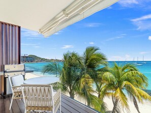 A balcony with a grill, white wicker chairs, and a view of the beach and ocean. - Breathtaking Beachfront Suite in Simpson Bay (Simpson Bay)