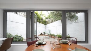 Ein Essbereich mit Tisch für vier Personen, großen Fenstern und Blick auf einen Garten.