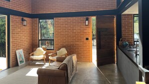 Quarto espaçoso com parede de tijolos, um sofá, duas cadeiras, um quadro e uma área de cozinha com fogão.
