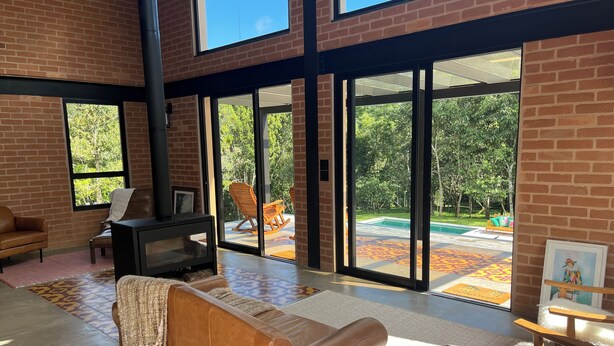 Uma sala de estar moderna com lareira, sofá de couro e grandes janelas com vista para uma piscina.