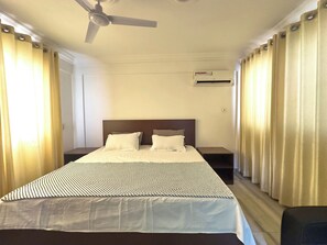 A hotel room with a bed, a ceiling fan, an air conditioning unit, and curtains. - LuxeHomes (Tema)