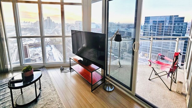 Ein modernes Wohnzimmer mit einem großen Fernseher, einem kleinen Tisch mit einer Pflanze und einem Balkon mit einem roten Sessel.