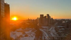Ein Stadtbild bei Sonnenuntergang mit Hochhäusern, einer Brücke und verschneitem Boden.