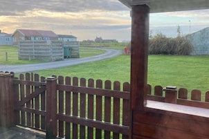 A view from a wooden structure with a gated entrance, a grassy field, and a road leading to a building with a red roof.