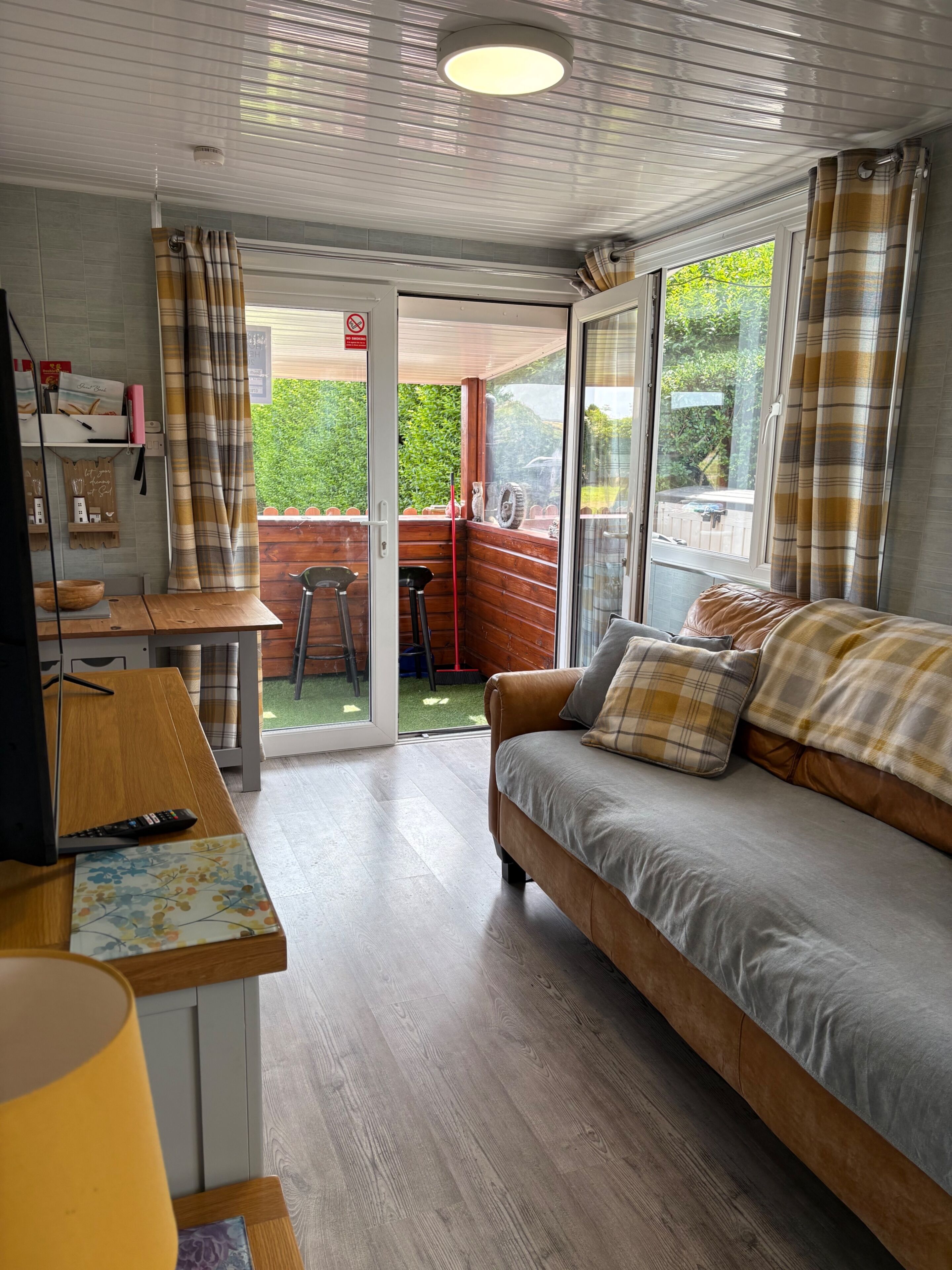 A cozy living area with a sofa, a wooden table, and a television. There is a sliding glass door leading to an outdoor space.