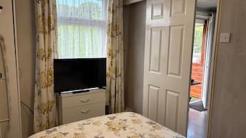 Quarto com cama, televisão sobre cômoda, porta e vista para o exterior.