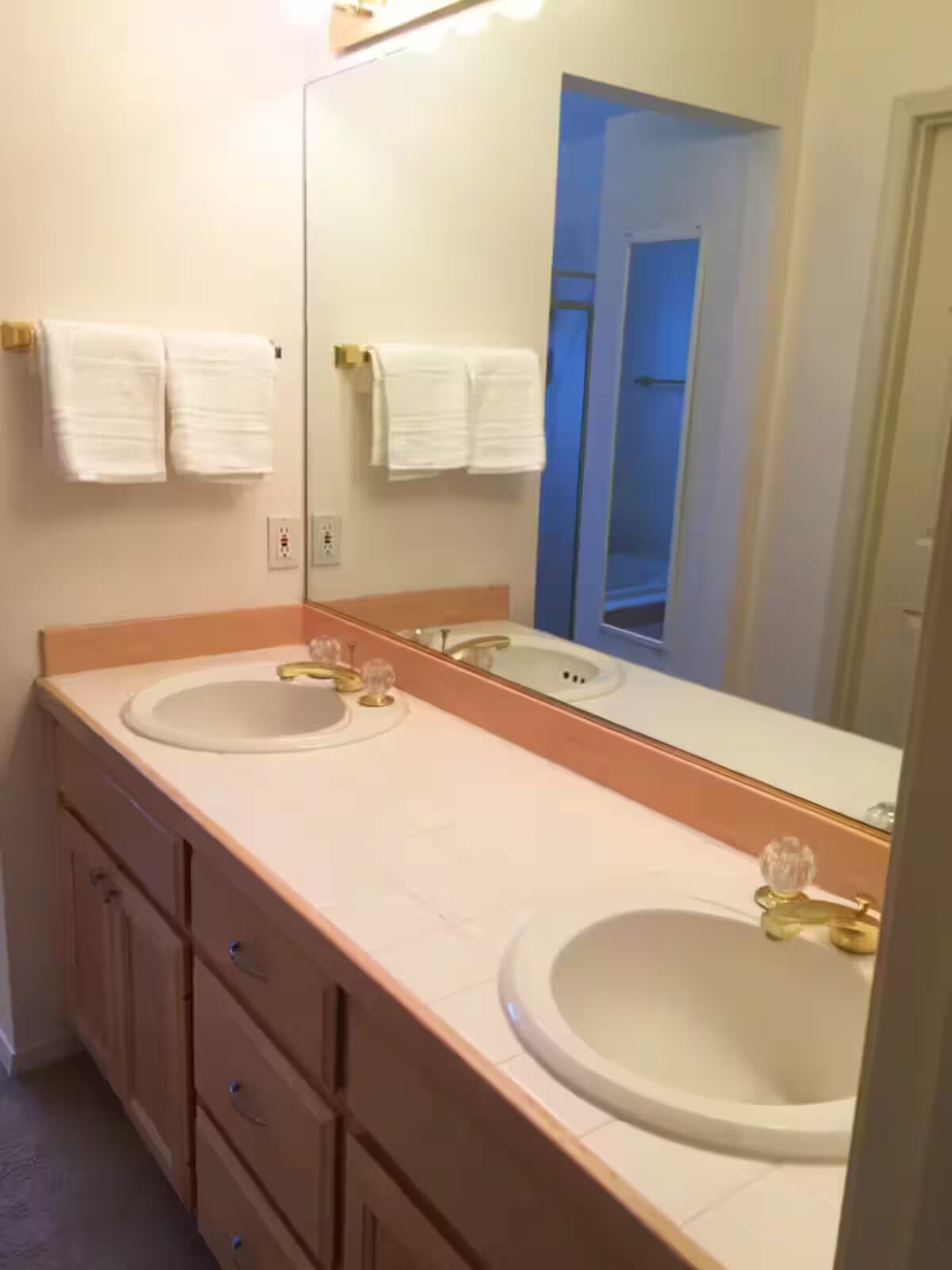 A bathroom with two sinks, a large mirror, and a door leading to another room.