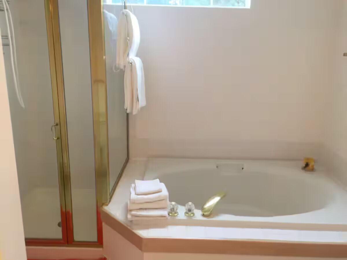 A bathroom with a glass shower enclosure, a bathtub, and a window.
