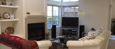 A living room with a fireplace, a TV, and two white sofas.