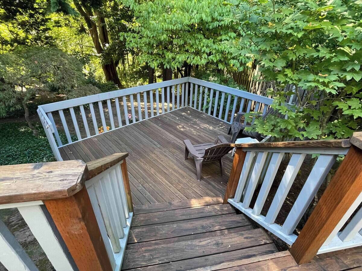 A wooden deck with a white railing, surrounded by greenery.