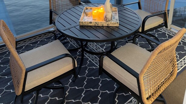 A balcony with a table and chairs, a decorative swan, and a view of a waterfront with buildings and boats. - Beautiful 3-bedroom Condo with a view for days in Lake Ozark, MO (Lake Ozark)