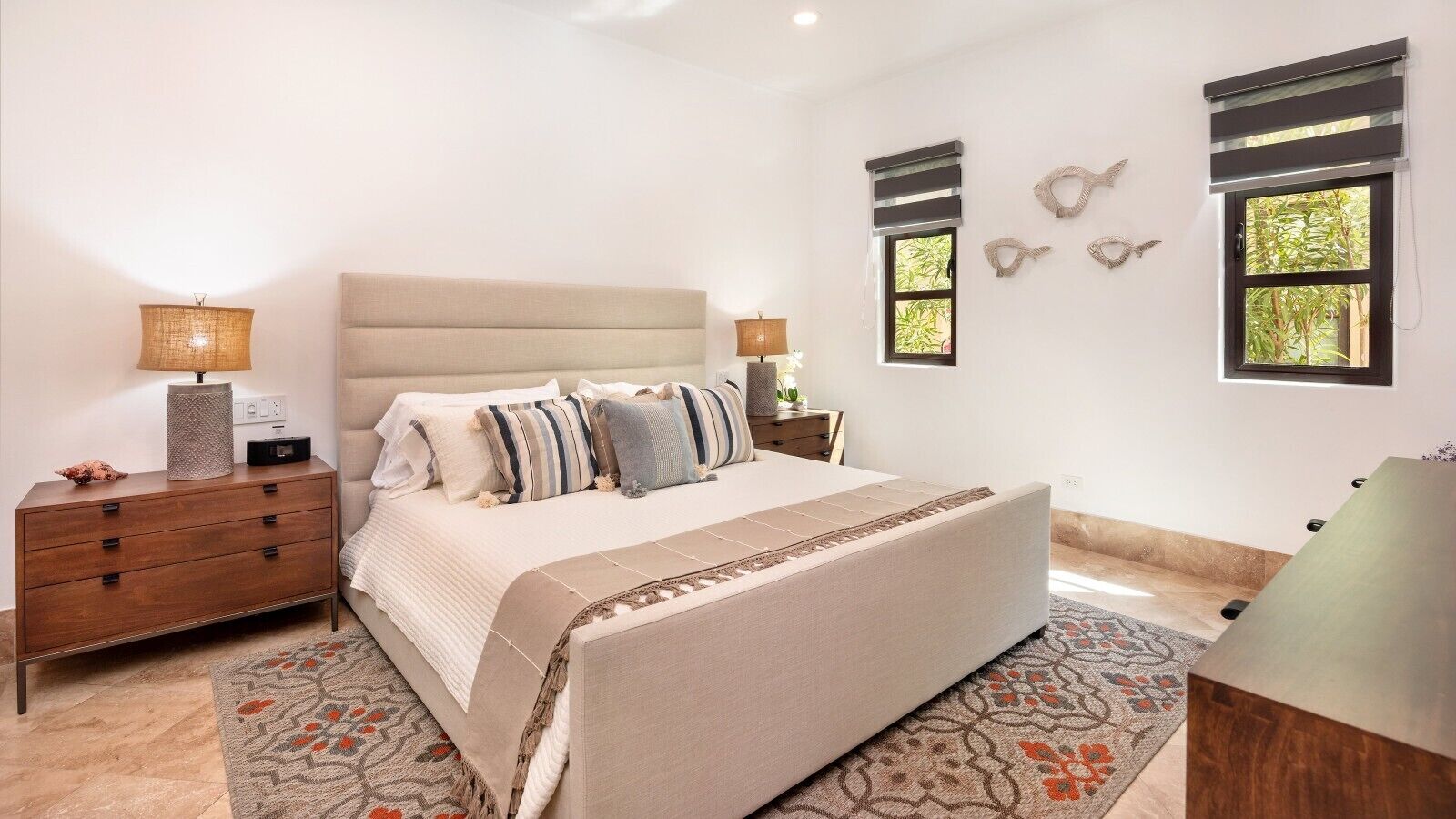 A bedroom with a bed, bedside tables, a dresser, a desk, and a window with blinds.