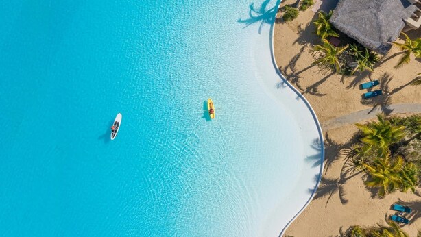An aerial view of a beach resort with a clear blue pool, a small boat, and palm trees. - Luxury Villa | Large Pool, Jacuzzi & Putting Green (Cabo San Lucas)