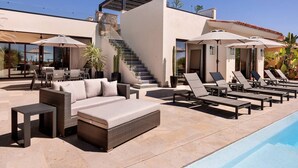 A modern outdoor pool area with lounge chairs, a sofa, and a staircase leading to an upper level. - Luxury Villa | Large Pool, Jacuzzi & Putting Green (Cabo San Lucas)