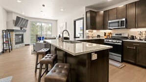 A modern kitchen with dark wood cabinets, a large island with stools, a built-in microwave, and a gas stove. - Hot Tubs | Near Ski Resort & Restaurants (Keystone)