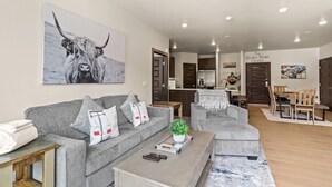 A modern living room with a grey sofa, a coffee table, and a dining area with wooden furniture. - Hot Tubs | Near Ski Resort & Restaurants (Keystone)