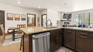 A modern kitchen with a dishwasher, granite countertop, dark cabinets, and a large window. - Hot Tubs | Near Ski Resort & Restaurants (Keystone)