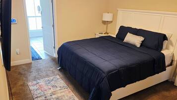 Un dormitorio con cama, mesita de noche, lámpara, puerta y alfombra.