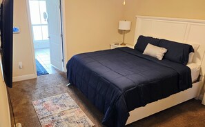 A bedroom with a bed, a nightstand, a lamp, a door, and a rug.
