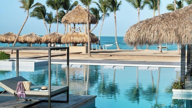 A pool area with lounge chairs, palm trees, and thatched-roof structures. - Finest Punta Cana (Punta Cana)