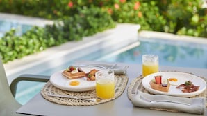 A dining table with breakfast plates, a glass of orange juice, and a poolside setting. - Finest Punta Cana (Punta Cana)
