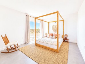 Ein Schlafzimmer mit einem Himmelbett, einem Schaukelstuhl, einem Teppich und Blick auf eine Wüstenlandschaft.