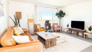 A living room with a sofa, chairs, a coffee table, a TV, and a large window. - Private 5-Acre Joshua Tree Desert Escape - Hot Tub, Fire Pit & Mountain Views (Landers)