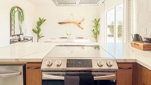 A modern kitchen with a stainless steel range hood, a built-in oven, and a large window providing natural light. - Private 5-Acre Joshua Tree Desert Escape - Hot Tub, Fire Pit & Mountain Views (Landers)