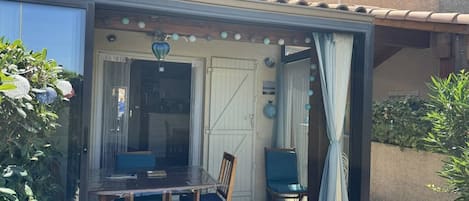 Eine überdachte Terrasse mit Tisch, Stühlen, einer Tür und einem kleinen Garten.