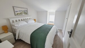 Ein Schlafzimmer mit einem Bett, einem Nachttisch, einer Lampe, einer grünen Tagesdecke und einem gerahmten Bild an der Wand.