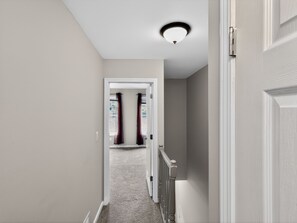 A hallway with a carpeted floor, a door on the right, and a ceiling light fixture. - Smyrna Townhome: 2 Queens, Patio, 13 Min to The Battery (Smyrna)