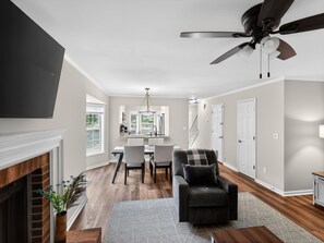 A modern living room with a fireplace, a dining area with a chandelier, and a ceiling fan. - Smyrna Townhome: 2 Queens, Patio, 13 Min to The Battery (Smyrna)