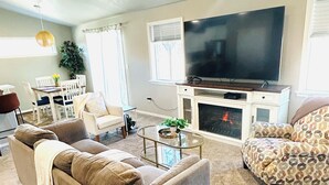 Ein Wohnzimmer mit Sofa, Sessel, Fernseher, Kamin und Essbereich.