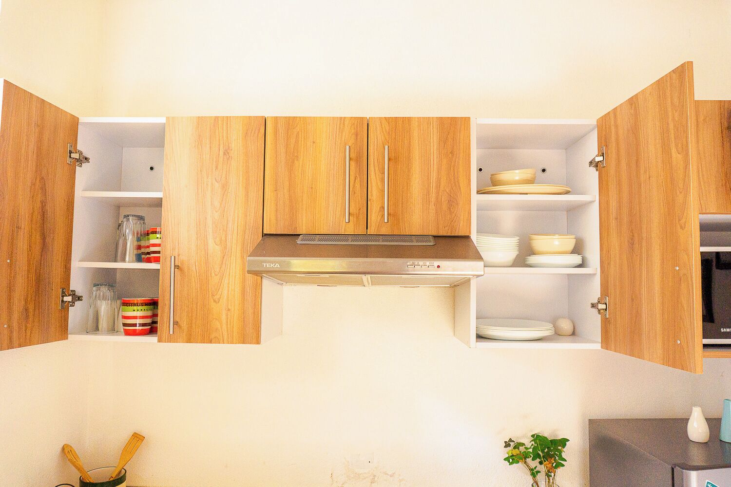 Une cuisine avec des meubles de rangement en bois, une hotte de cuisinière en acier inoxydable et des étagères remplies d’assiettes et de bocaux.
