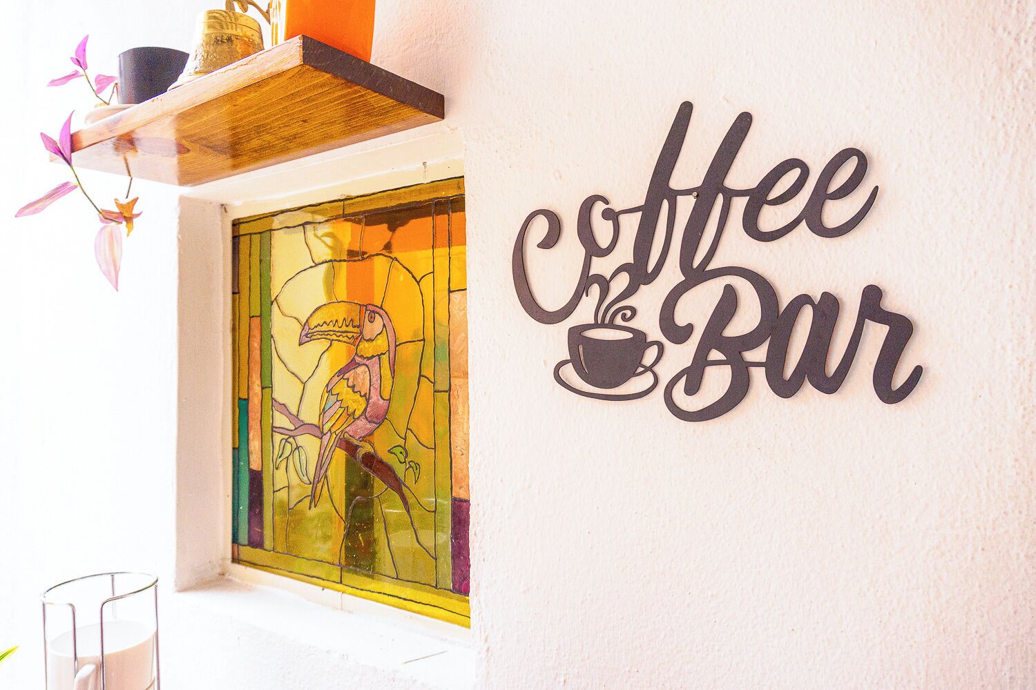 Un mur sur lequel on peut lire l’inscription « Coffee Bar », et une fenêtre à vitraux représentant un toucan.