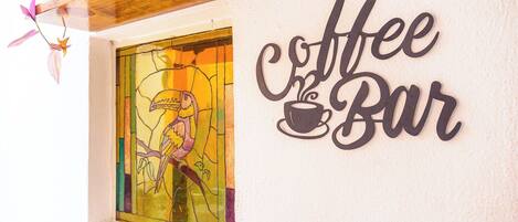 Un mur sur lequel on peut lire l’inscription « Coffee Bar », et une fenêtre à vitraux représentant un toucan.