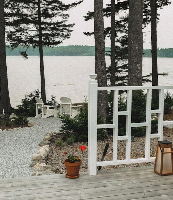 A deck with Adirondack chairs, a white fence, and a view of a lake. - Slow-Luxury Oceanfront Hot Tub, Sunset, and Dogs OK (Friendship)
