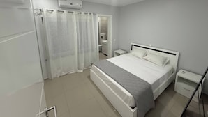 A bedroom with a bed, nightstands, a mirror, a shower, and an air conditioning unit.