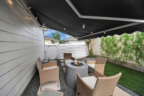 An outdoor patio with wicker furniture, a round table with a fire pit, and a black canopy.