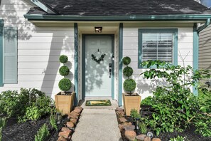 A house with a front door, a mailbox, and a small garden with potted plants and a doormat.