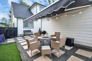 An outdoor patio with a fire pit, wicker furniture, and a string of lights. - Boutique Stay | Prvt Lounge, Arcade, Firepit | 15m IAH (Houston)