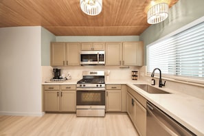 A modern kitchen with wooden cabinets, stainless steel appliances, a double sink, and pendant lighting. - Boutique Stay | Prvt Lounge, Arcade, Firepit | 15m IAH (Houston)